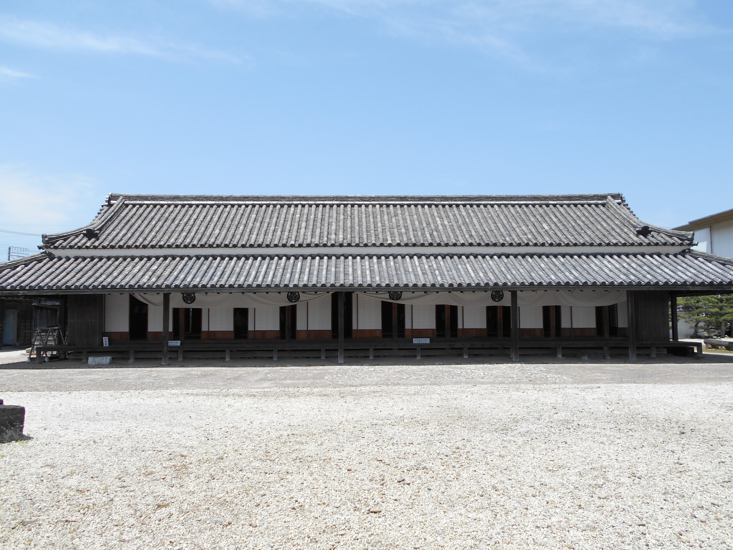 青空の下、広々とした白砂利の敷地に建つ新居関跡（あらいのせきあと）の建物正面。