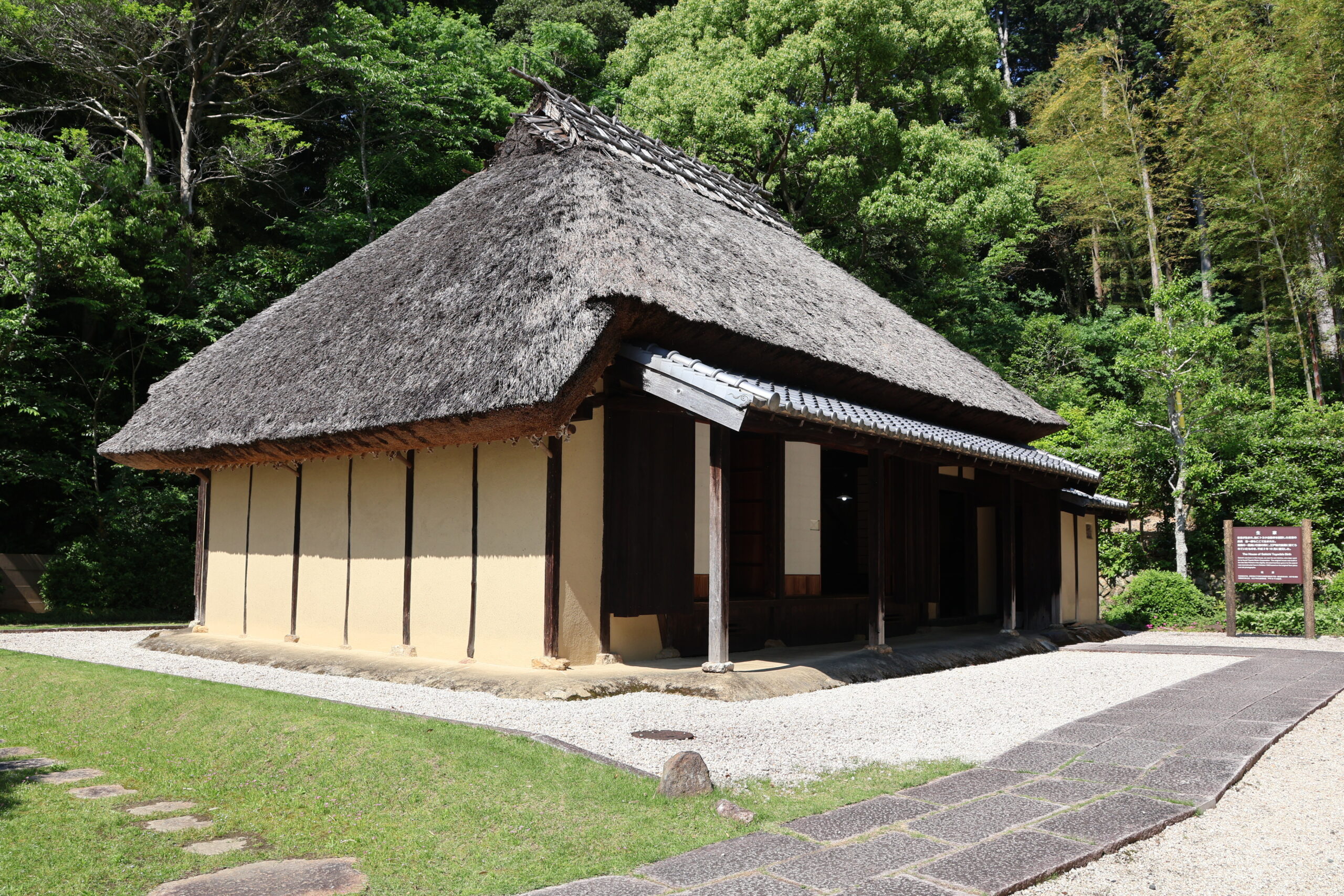豊田佐吉記念館に復元された豊田佐吉の生家（1990年復元）の外観。茅葺き屋根の伝統的な建物が緑に囲まれて建つ